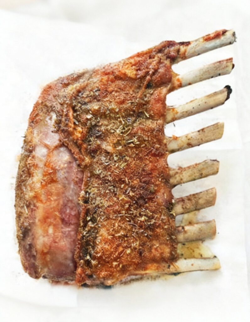 Golden roasted lamb rack with crispy crust and fresh herbs, served as an elegant main dish.